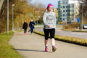 Ronneby, Sweden - April 3, 2016: Young adult woman power walking on a pedestrian walkway in town. She wears earphones and looks concentrated.